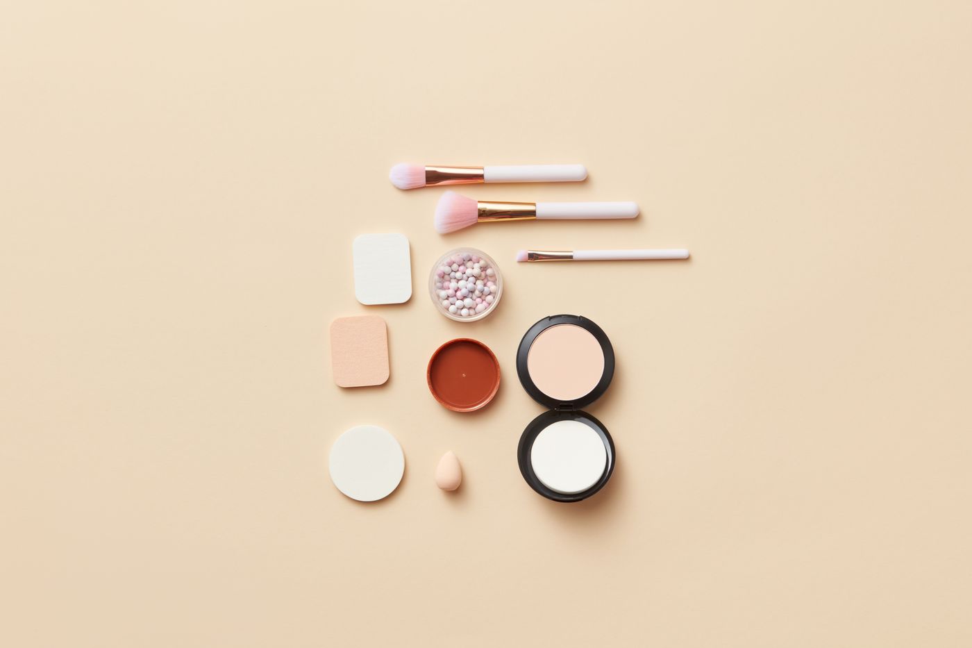 Productos de maquillaje en tonos neutros sobre fondo beige