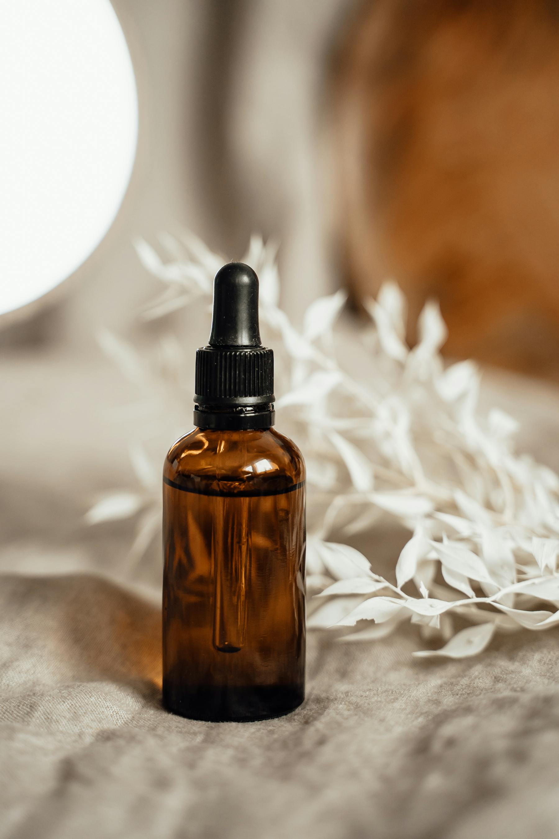 Frasco ambar de serum sobre tela clara con flores secas